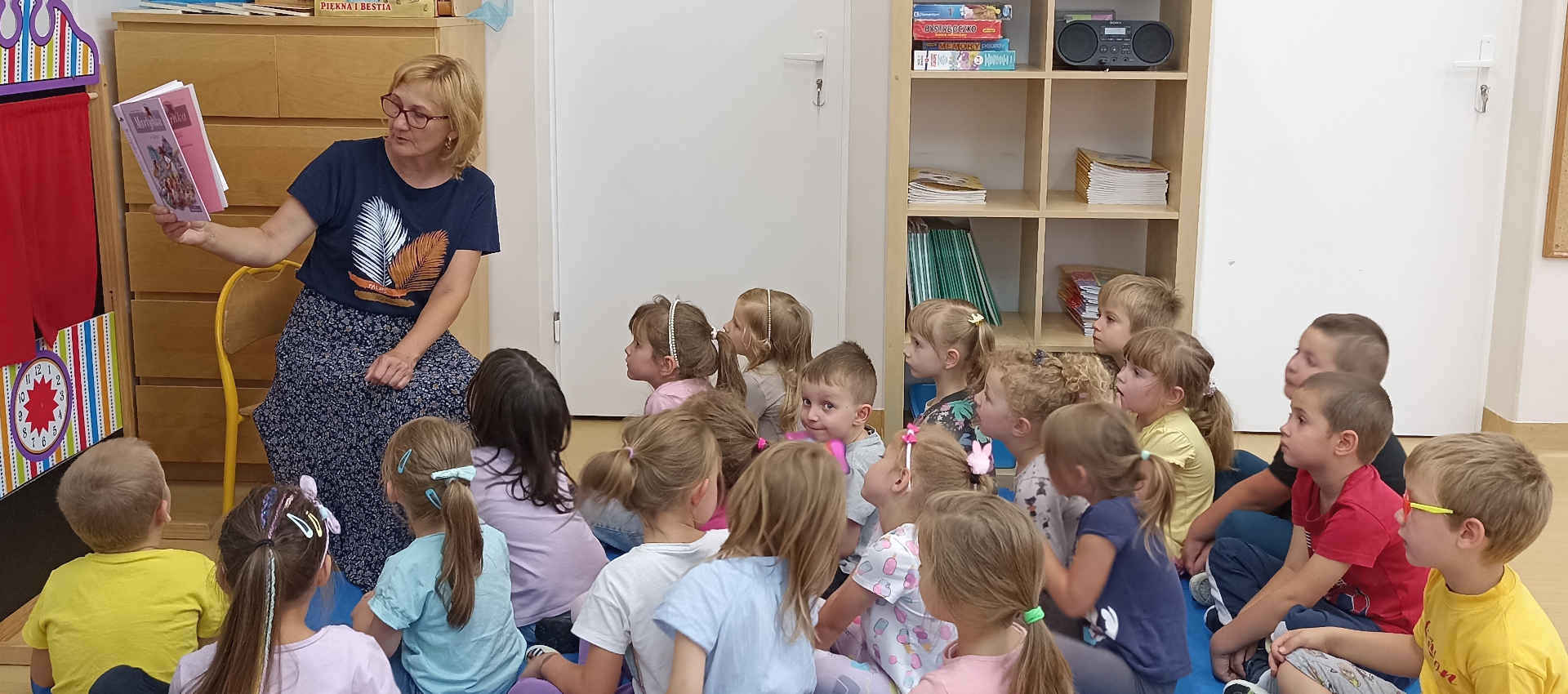 Dzieci słuchają opiekunki, która czyta im książkę