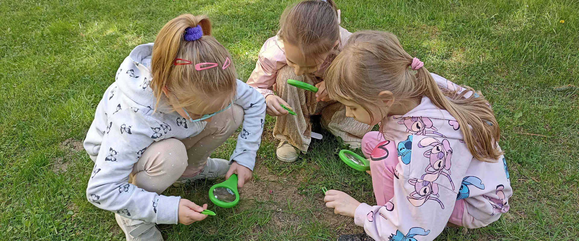 Dziewczynki z lupami szukają żyjątek w trawie