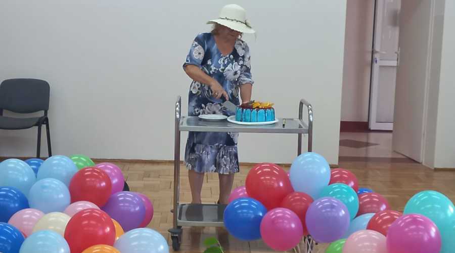 Kobieta kroi torta, naokoło kolorowe balony